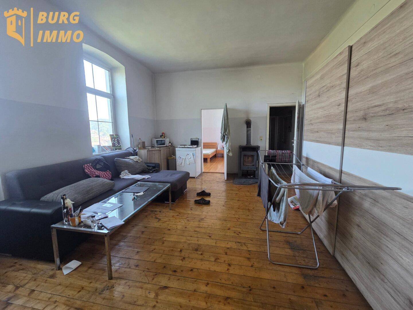Geräumiges Wohnzimmer mit Holzdielenboden, Sofa, Kaminofen und Blick in einen weiteren Raum.