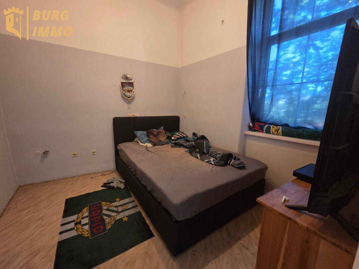 Schlafzimmer mit Doppelbett, dunklen Vorhängen und einem Fernseher, gemütlich eingerichtet.
