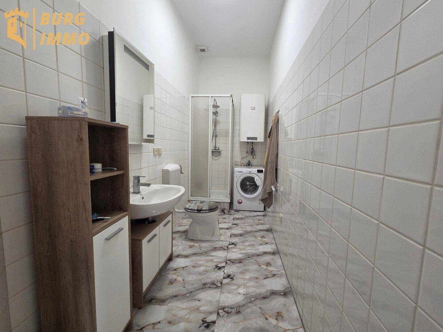Modern gefliestes Badezimmer mit Waschtisch, Dusche und Waschmaschine, mit Marmoroptik-Bodenfliesen.
