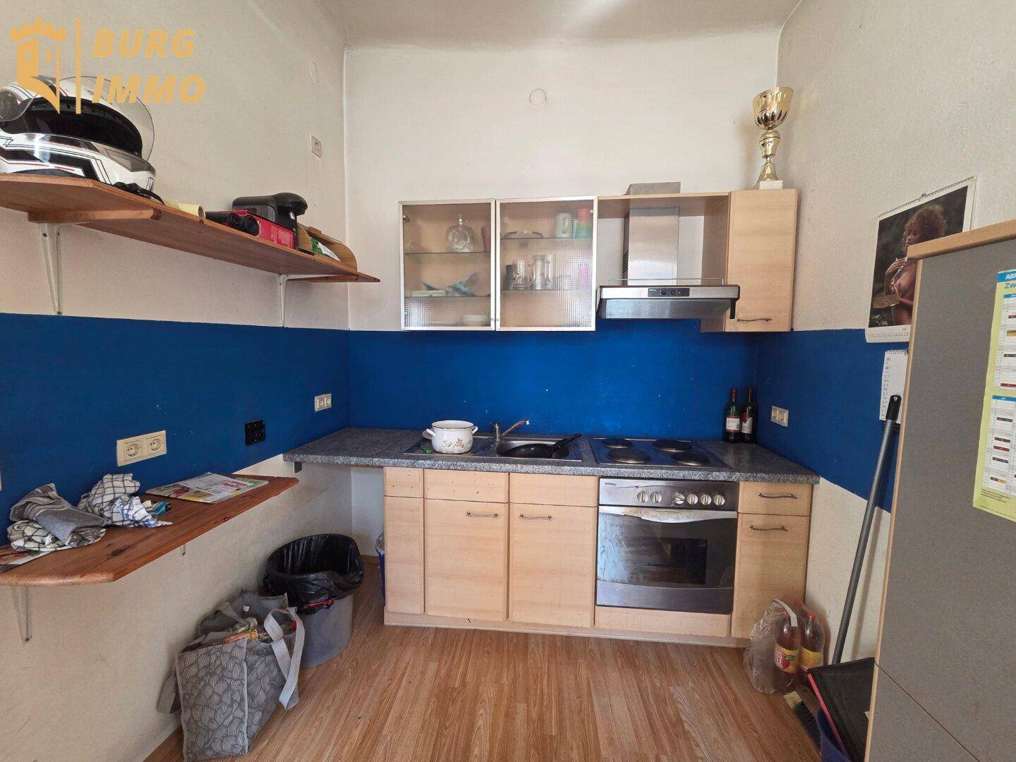 Kleine Küche mit blauer Rückwand, Holzschränken, Spüle und Herd mit Backofen.