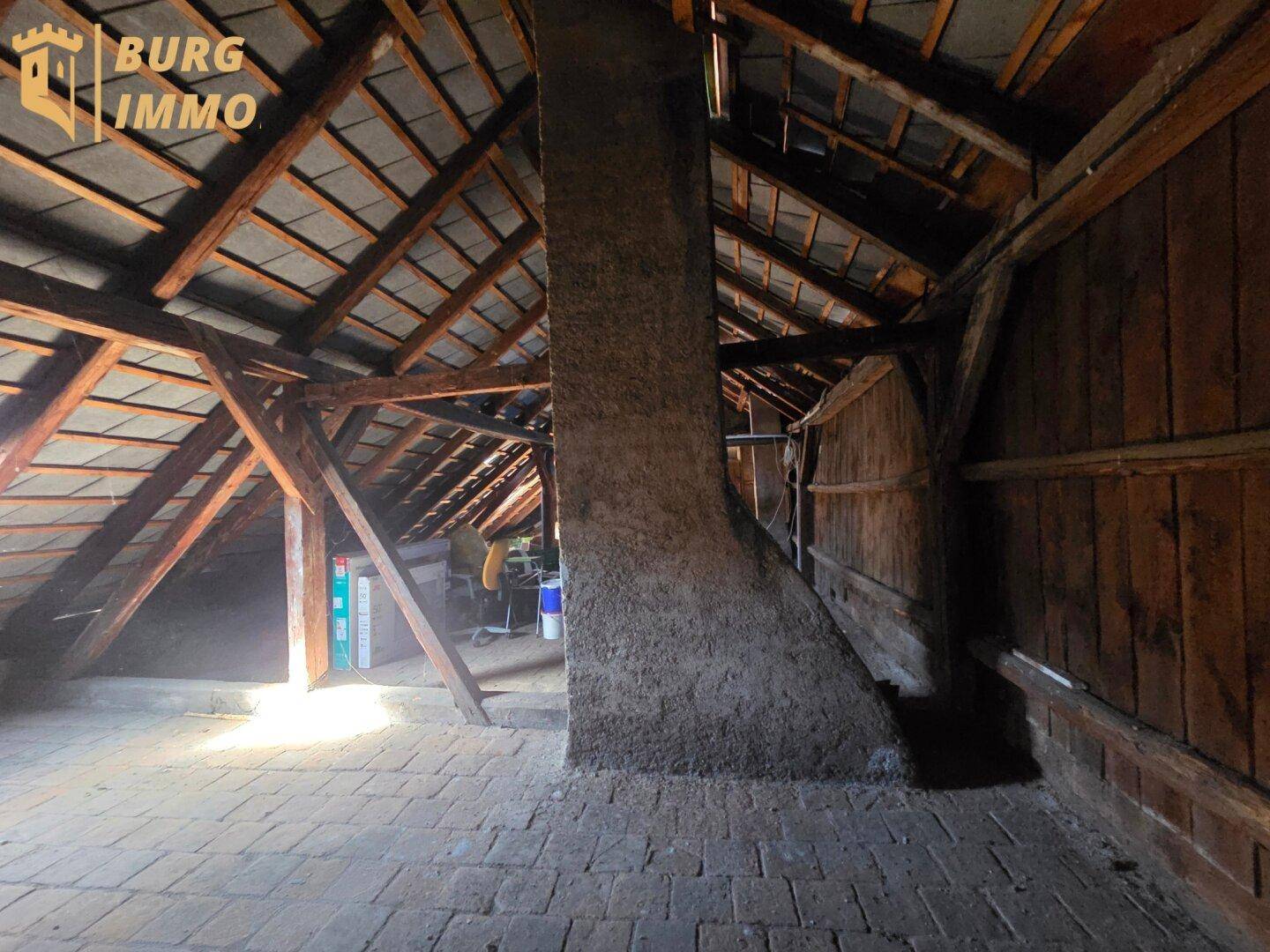 Unausgebauter Dachboden mit sichtbaren Holzbalken und Ziegelboden, bietet Ausbaupotenzial.