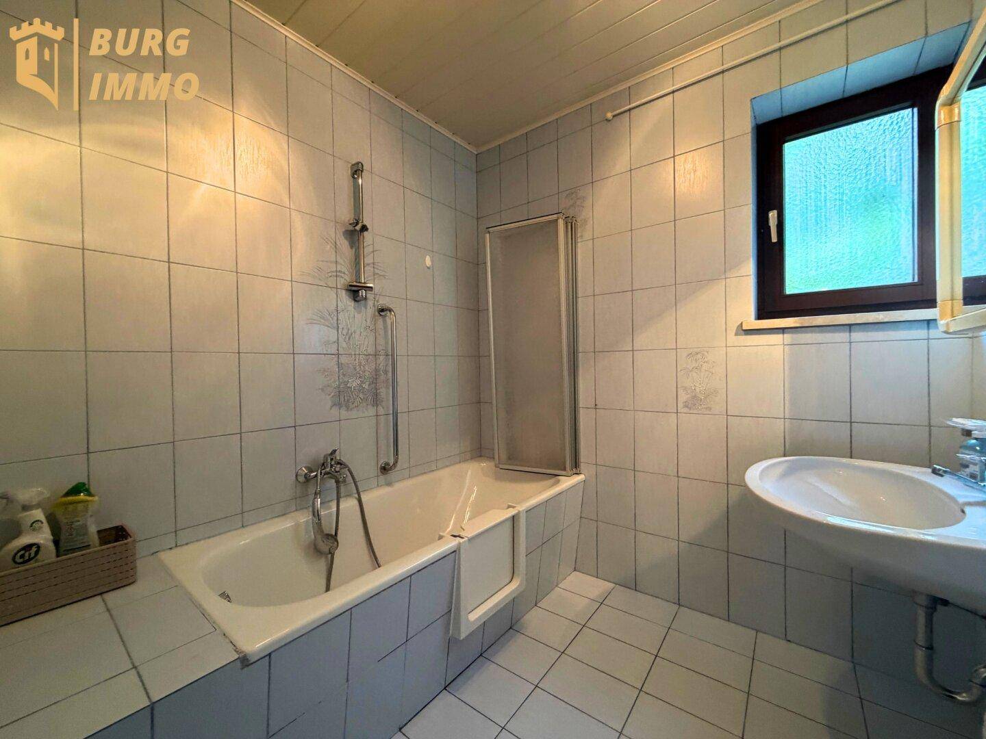 Badezimmer mit Badewanne, Dusche und hellblauen Fliesen.