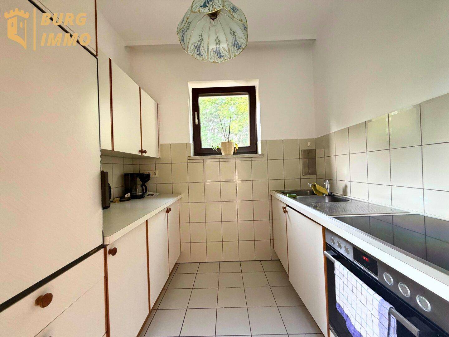 Funktionale Küche mit weißen Schränken, Fliesenboden und Fenster.