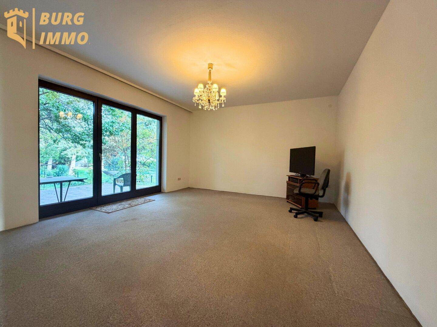 Helles Wohnzimmer mit Teppichboden und großen Fenstern zum Garten.