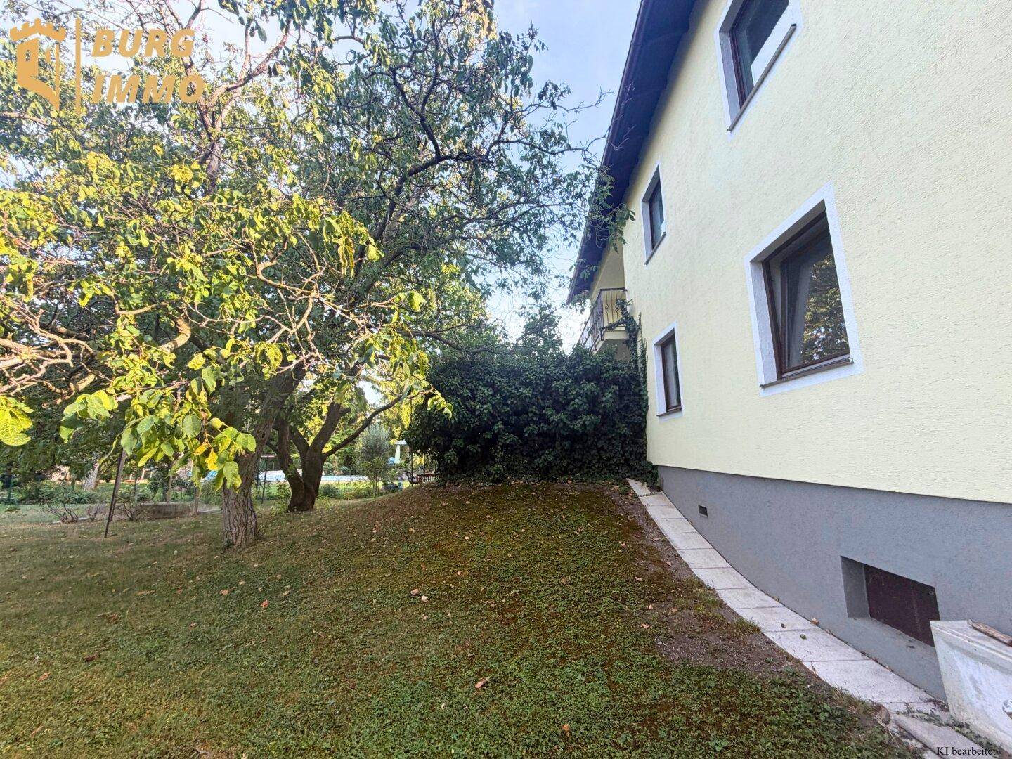 Seitenansicht des Hauses mit üppigem Grün und Gartenbereich im Sonnenlicht.