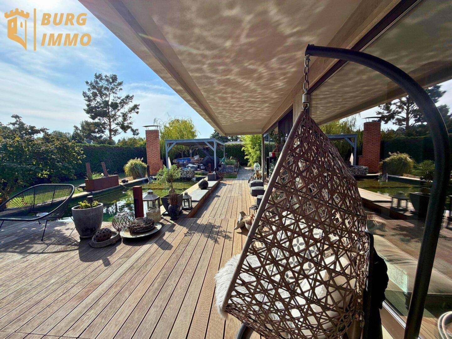Weitläufige Holzterrasse mit Hängesessel und Blick auf den Garten, ideal für Entspannung im Freien.
