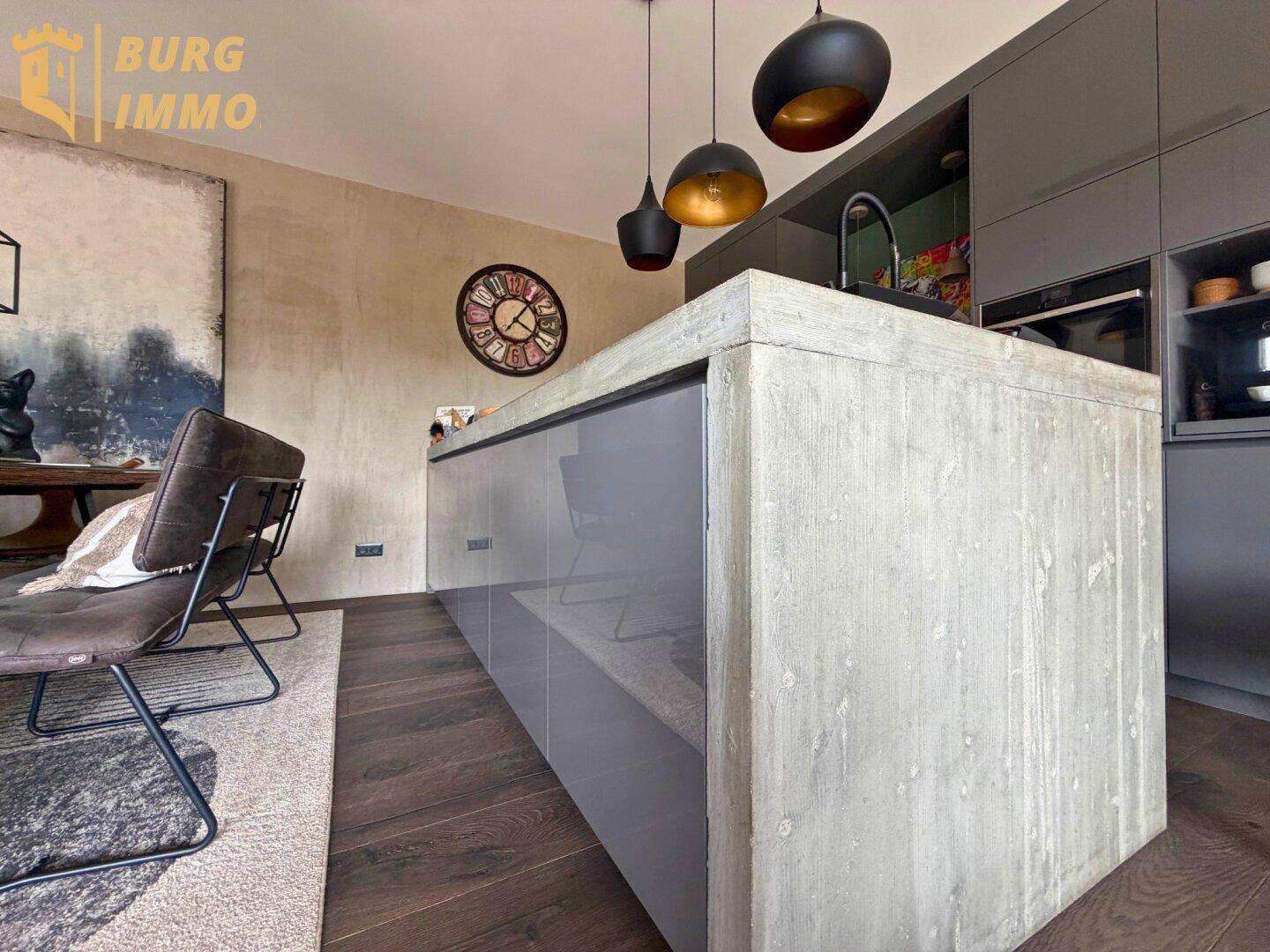 Moderne Küche mit grauen Fronten, Kücheninsel aus Betonoptik und dunklem Holzboden.