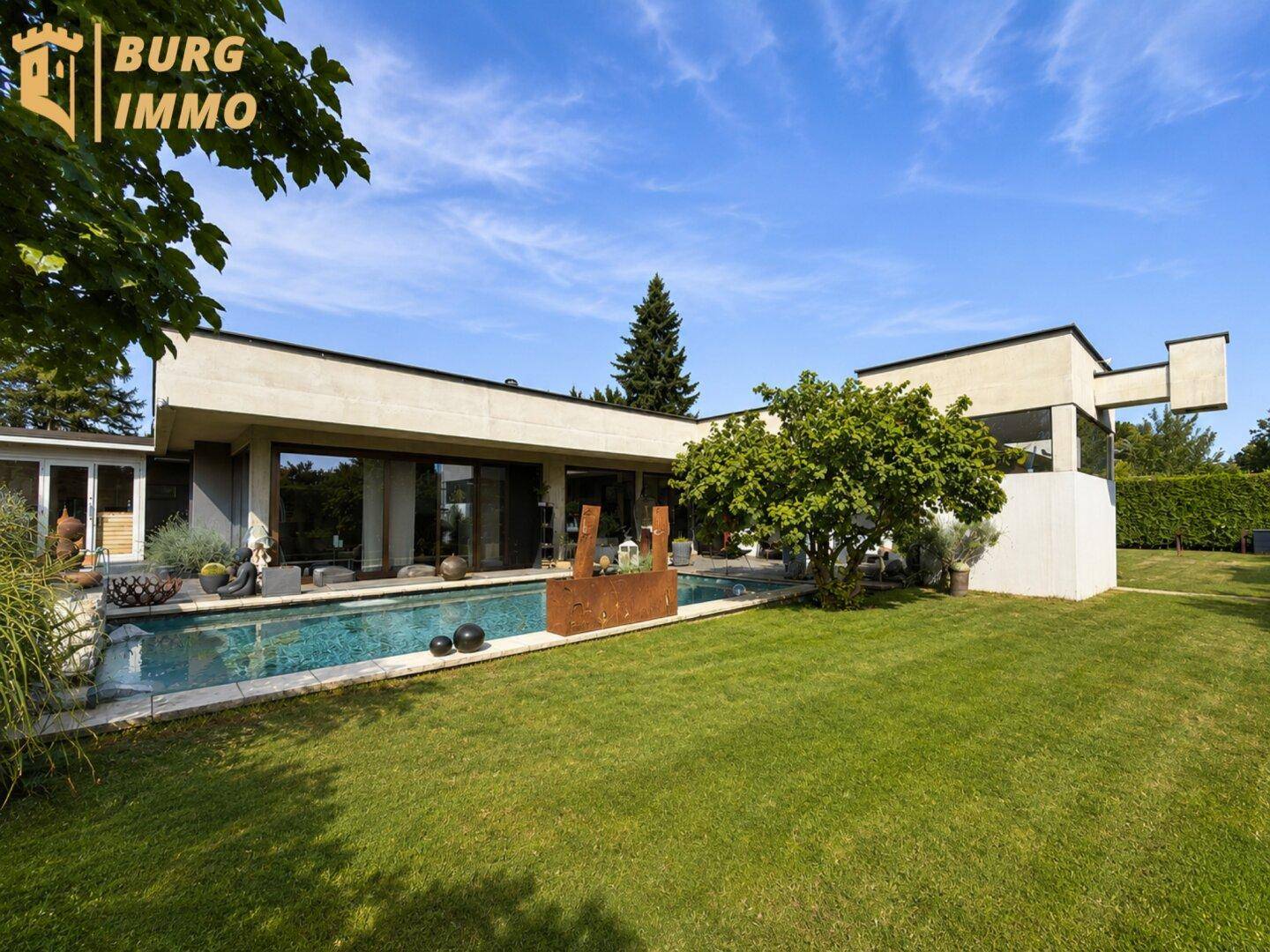 Großzügiger Gartenbereich mit modernem Haus, Pool und weitläufiger Rasenfläche unter blauem Himmel.