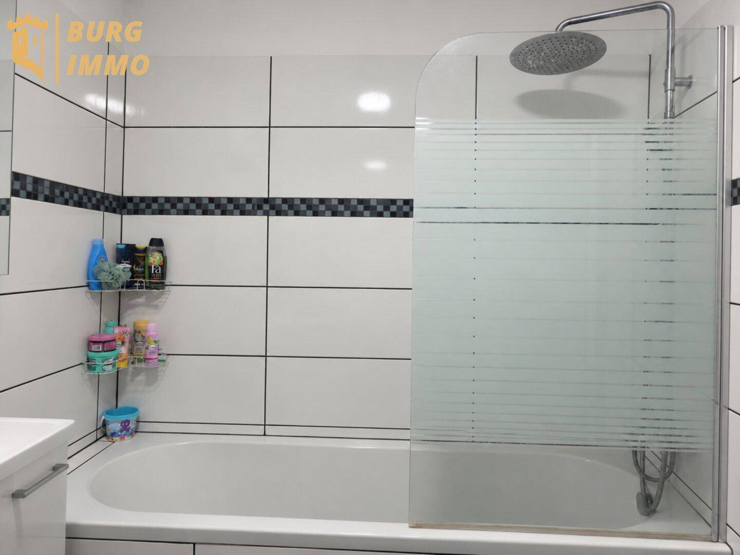 Badezimmer mit Badewanne, Duschabtrennung und Regendusche, umgeben von weißen Fliesen.