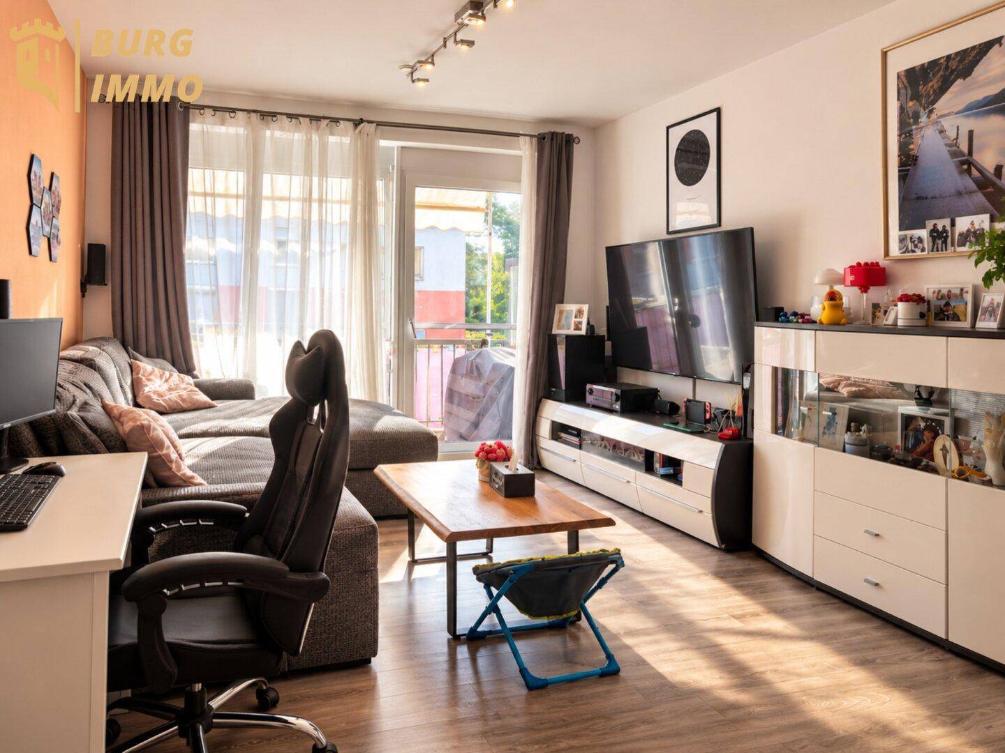 Geräumiges Wohnzimmer mit bequemer Couch, großem Fernseher und hellem Laminatboden.