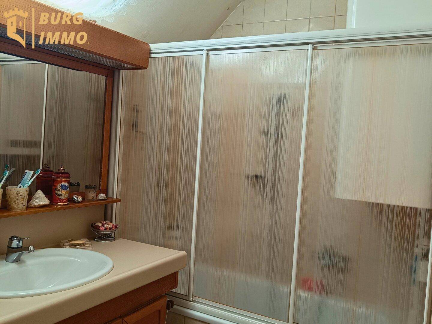 Badezimmer mit Waschbecken, Spiegel und Duschkabine mit Schiebetüren.