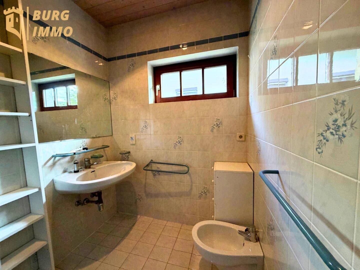Badezimmer mit hellen Fliesen, Einzelwaschbecken, Bidet und Fenster.
