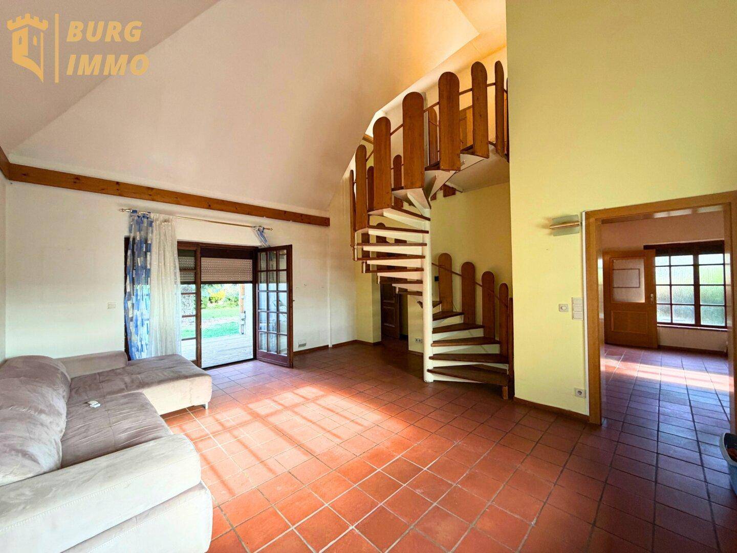 Helles Wohnzimmer mit Terrakotta-Fliesenboden, Holzwendeltreppe und Zugang zum Garten.