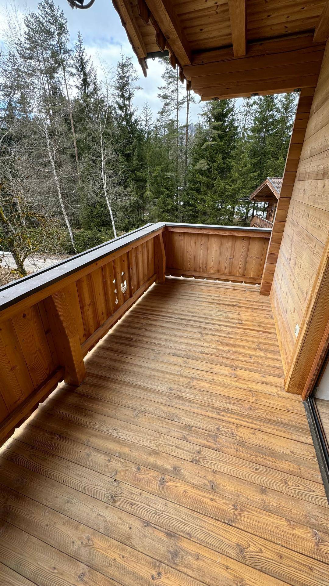 Geräumiger Holzbalkon mit Panoramablick auf die umliegende Berglandschaft und dichte Wälder.
