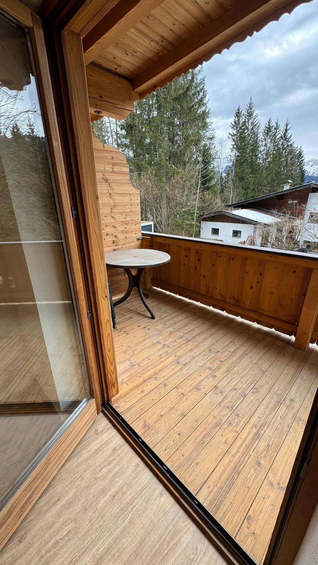 Gemütlicher Holzbalkon mit kleinem Tisch und Blick ins Grüne, perfekt für entspannte Stunden im Freien.