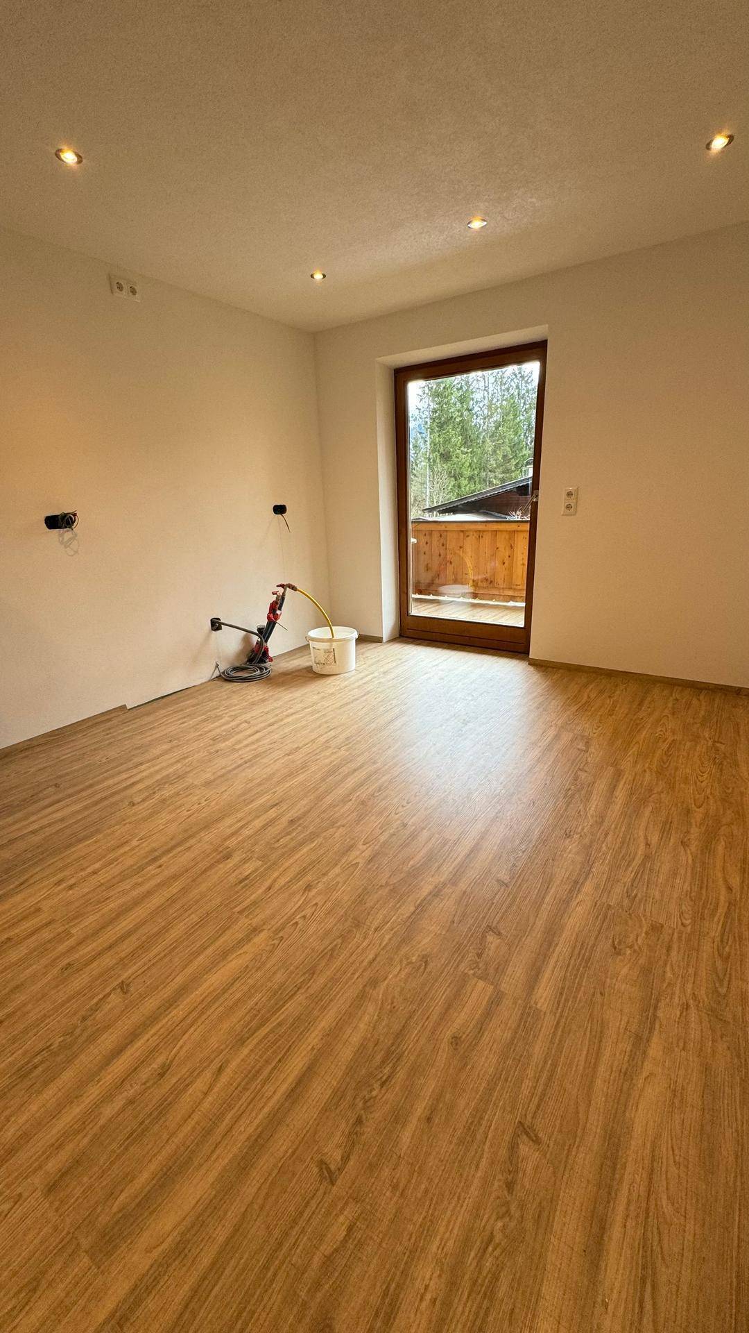 Leerer Raum mit neuem Laminatboden, weißen Wänden und Zugang zu einem Außenbereich, bereit für die Einrichtung.