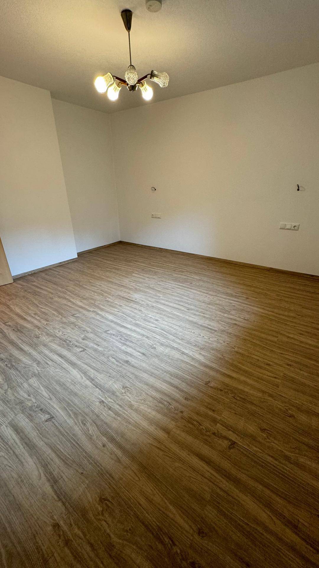 Geräumiger, leerer Raum mit hellem Laminatboden und weißen Wänden, ideal für individuelle Gestaltungsmöglichkeiten.