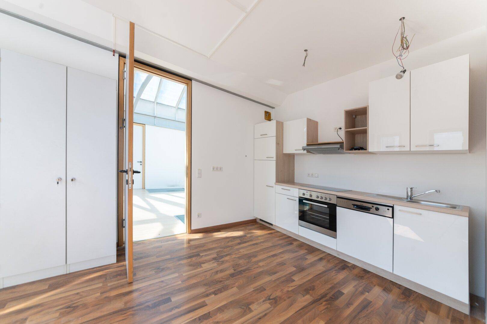 Neue Einbauküche mit weißen Schränken, Holzarbeitsplatte und Blick in den hellen Loftbereich.