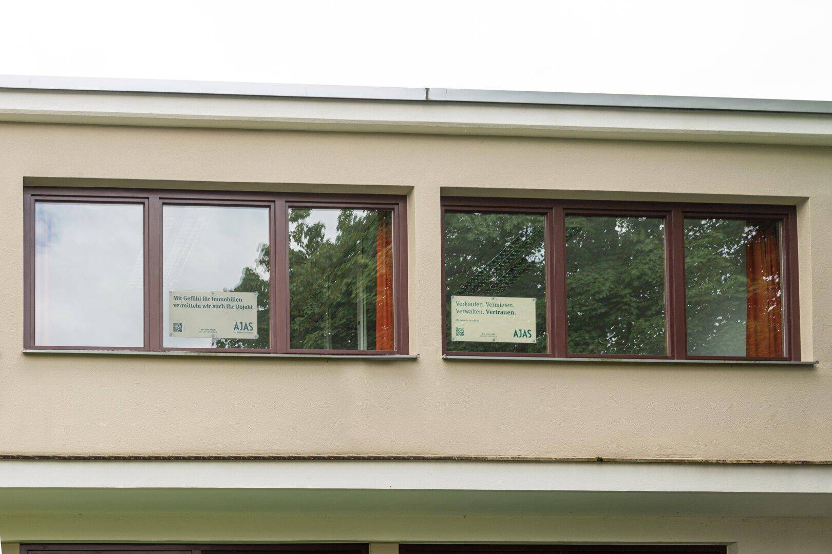 Nahaufnahme einer Gebäudefassade mit braunen Fensterrahmen und beiger Wandfarbe.