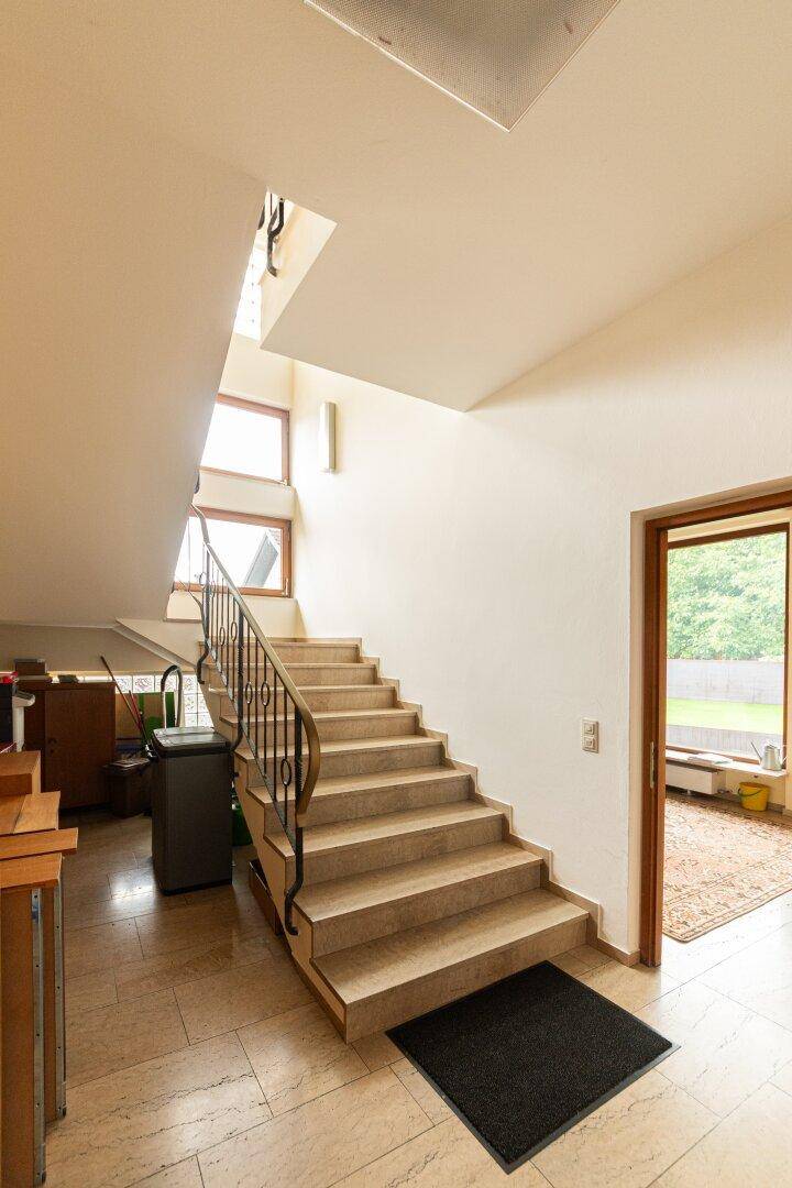 Helles Treppenhaus mit Steinfliesen und schmiedeeisernem Geländer, das zu den oberen Etagen führt.