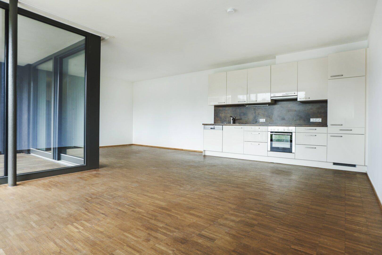 Geräumiger Wohnbereich mit moderner Einbauküche, Parkettboden und großen Fenstern.