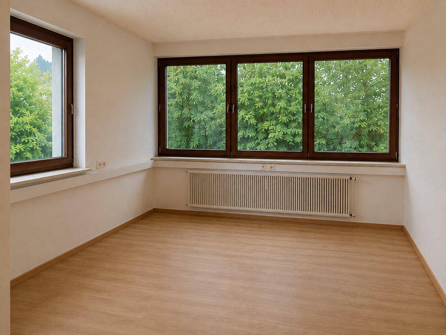 Unmöblierter Raum mit großen Fenstern, Heizkörper und hellem Laminatboden.