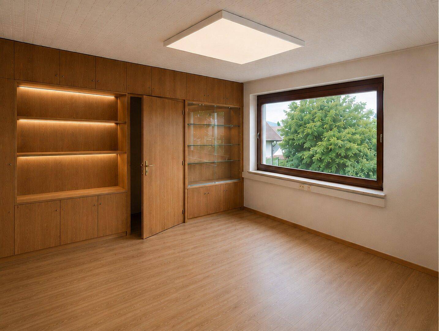 Leerer Raum mit Einbauschränken aus Holz, Laminatboden und Blick ins Grüne.