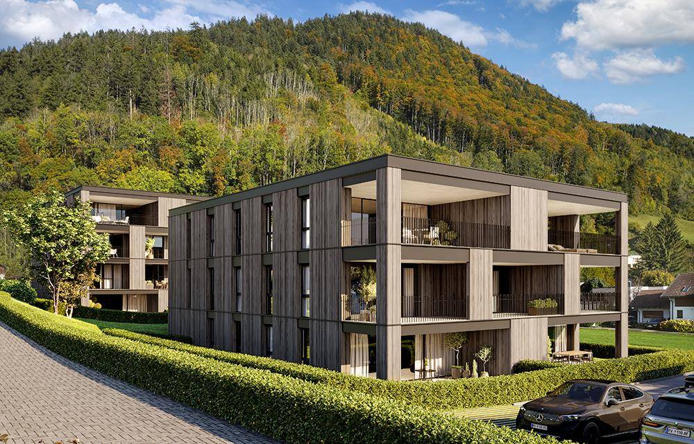 Moderne Wohngebäude mit Holzfassade und Balkonen, eingebettet in die grüne Hügellandschaft mit Weitblick.