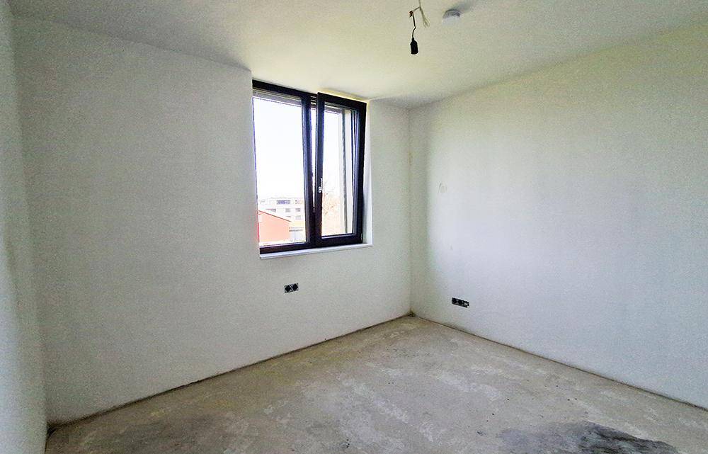 Unmöblierter Raum im Rohbauzustand mit Fenster und weiß gestrichenen Wänden.
