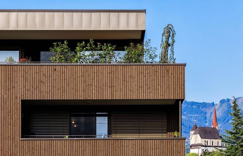 Moderne Holzfassade mit Balkonen und einem traditionellen Kirchturm im Hintergrund.