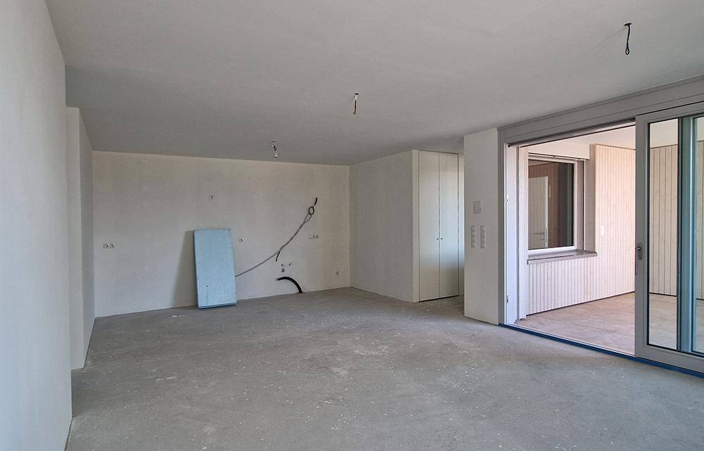 Unfertiger Wohnbereich mit Betonboden und Zugang zu einem Außenbereich, bereit für den Ausbau.