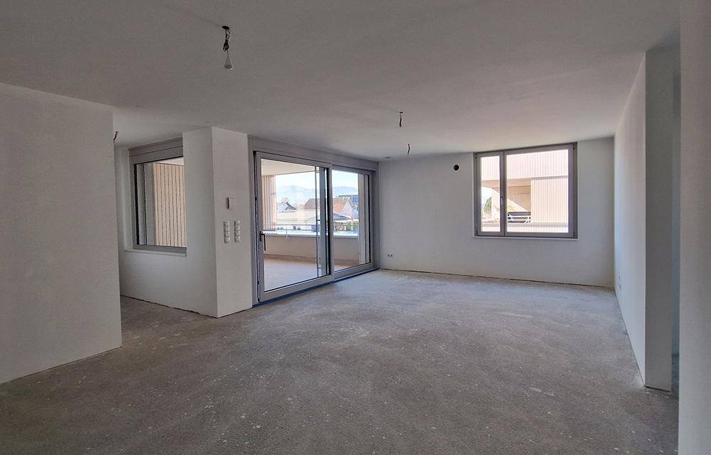 Geräumiger, unmöblierter Raum mit großen Fenstern und Schiebetüren zu einem Balkon oder einer Terrasse.