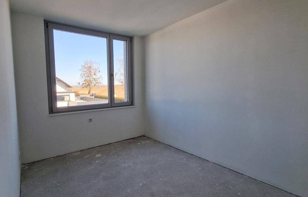 Unmöbliertes Schlafzimmer im Rohbau mit einem Fenster und Blick ins Grüne.