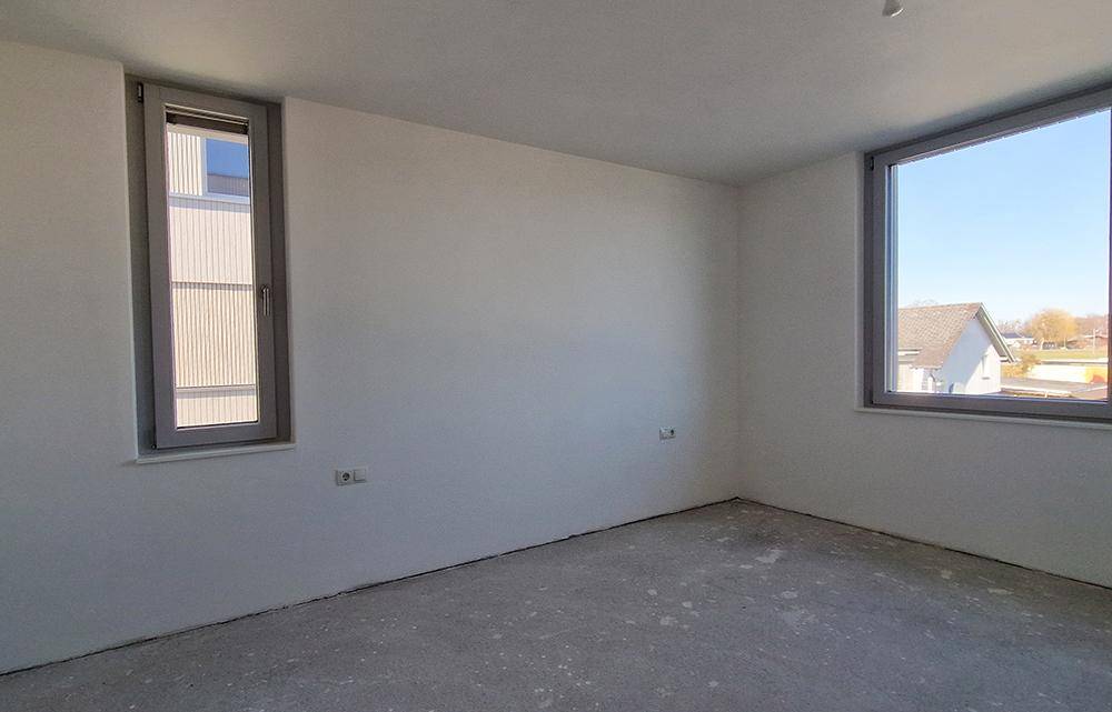 Helles, unmöbliertes Zimmer im Rohbau mit zwei Fenstern, ideal als Schlaf- oder Arbeitszimmer.