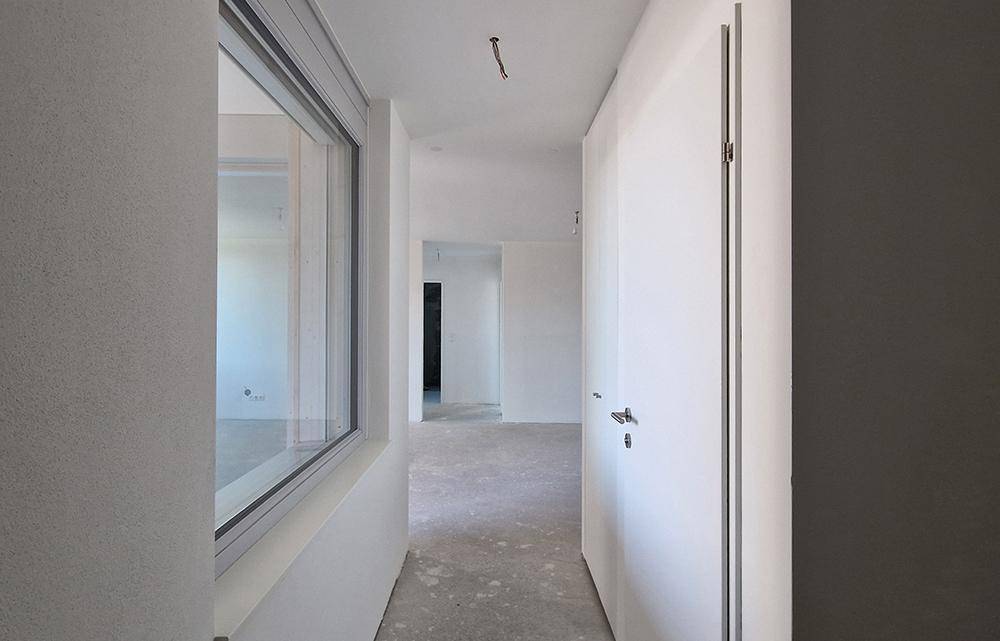 Unfertiger Flur im Rohbau mit einer Tür und einem Fenster, das Licht hereinlässt.