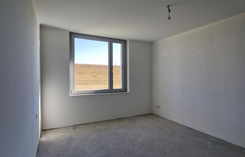 Heller, unmöblierter Raum im Rohbau mit einem Fenster und Blick auf eine grüne Landschaft.