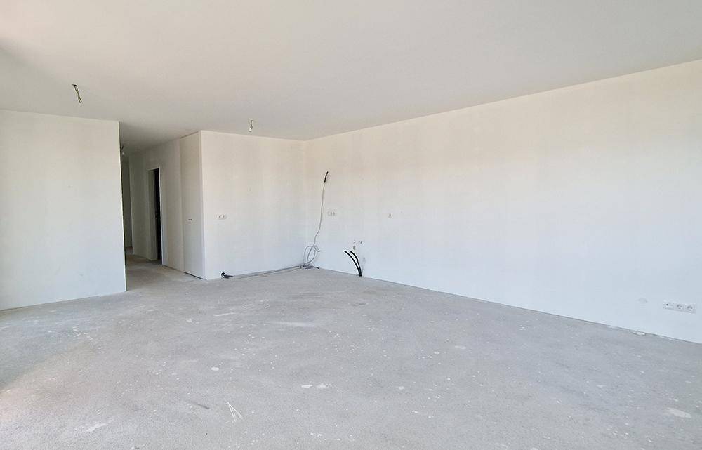 Leerer, heller Innenraum im Rohbau mit weißen Wänden und unfertigem Betonboden.