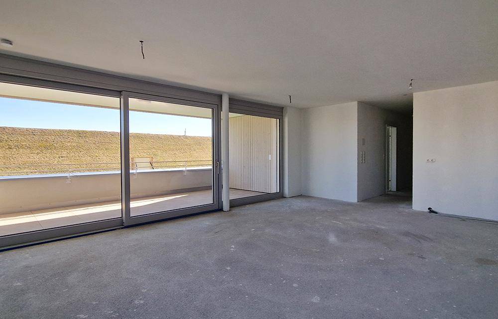 Großer, heller Raum im Rohbau mit Schiebetüren zum Balkon und weitem Blick ins Grüne.