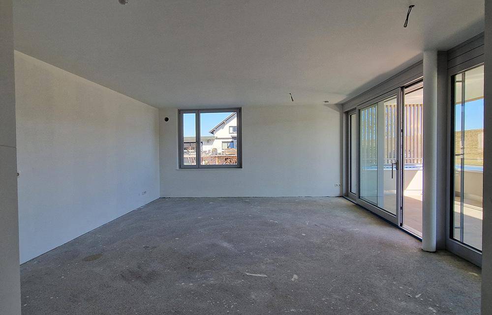 Heller, unmöblierter Raum im Rohbau mit großen Schiebetüren zum Außenbereich und einem Fenster.