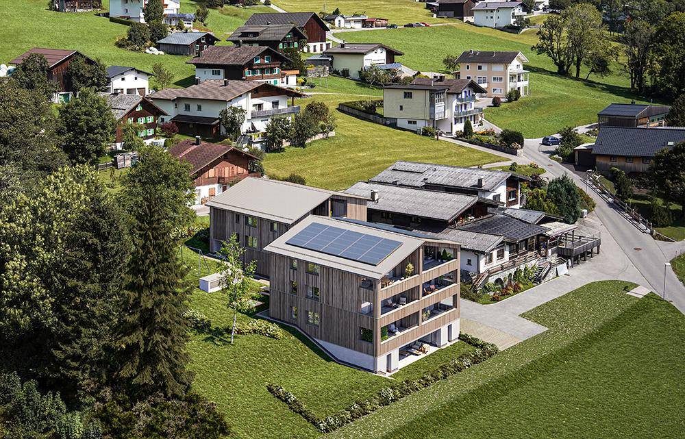 Modernes Holzgebäude mit Solarpaneelen auf dem Dach, eingebettet in eine grüne Hügellandschaft.