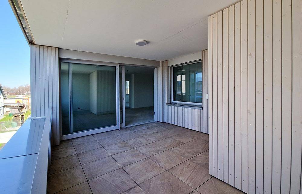 Geräumiger Balkon mit Fliesenboden und Zugang zu hellen Innenräumen.