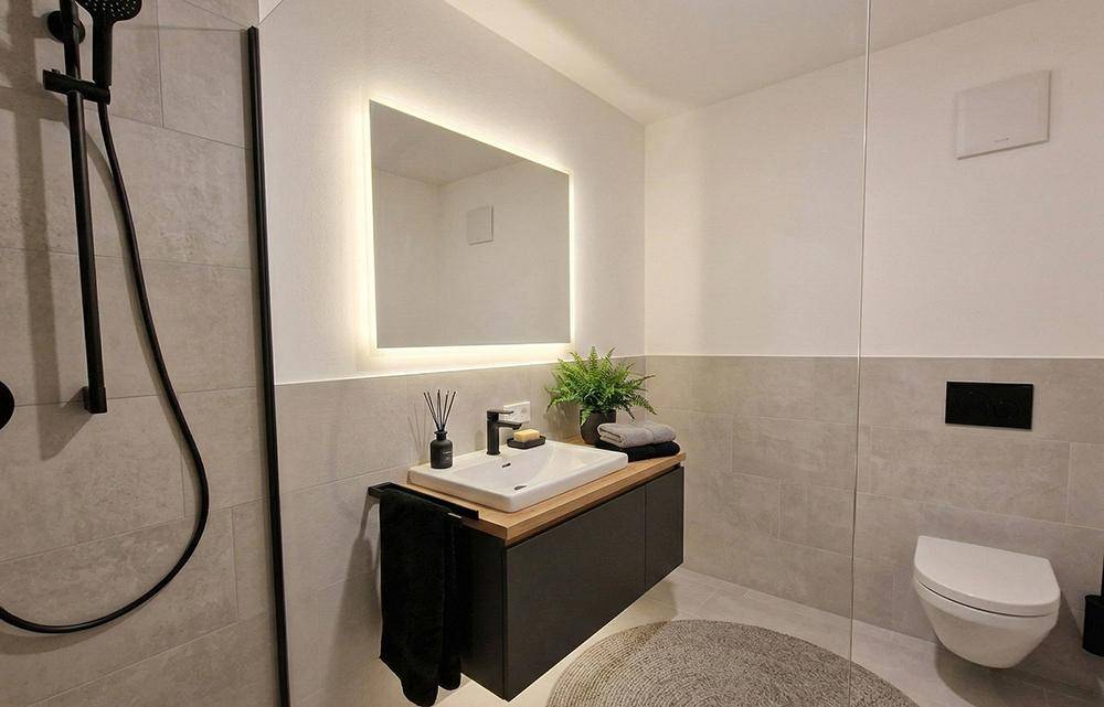 Modernes Badezimmer mit begehbarer Dusche, schwebendem Waschtisch und beleuchtetem Spiegel.
