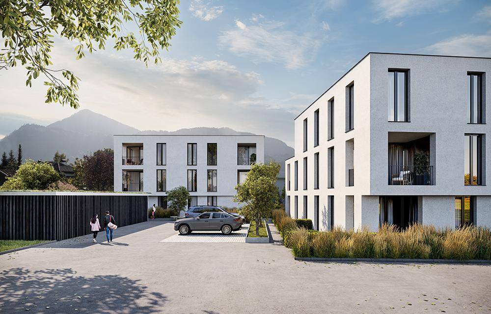 Moderne Wohngebäude mit Parkplätzen und Grünflächen vor einer Bergkulisse.