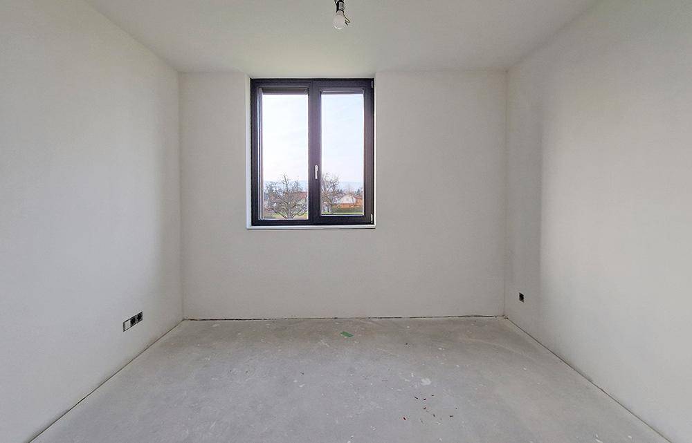 Unfertiger Raum im Rohbauzustand mit Fenster und Betonboden.