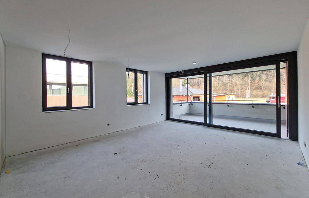 Unfertiger Raum im Rohbauzustand mit großem Fenster und Balkonzugang.