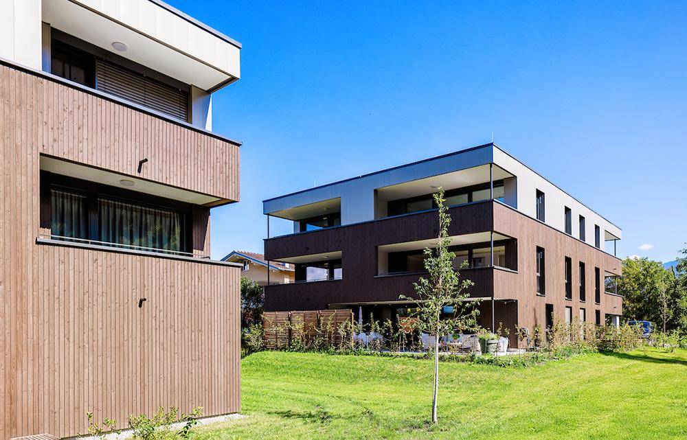 Moderne Wohnanlage mit Holzfassade, Balkonen und gepflegter Grünfläche.