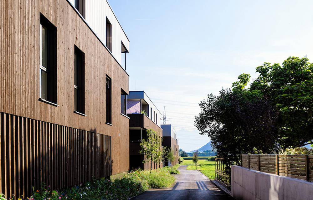 Moderne Wohnanlage mit Holzfassade, Wegen und grüner Landschaft im Hintergrund.