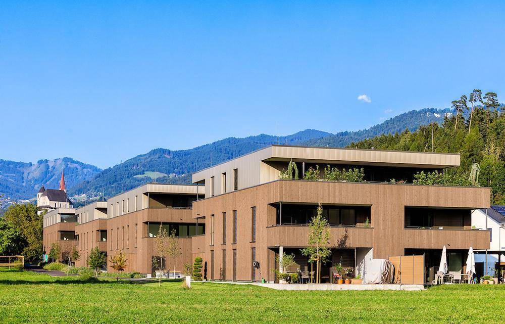 Moderne Wohnanlage mit Holzfassade, Balkonen und weitem Blick auf die Berge.