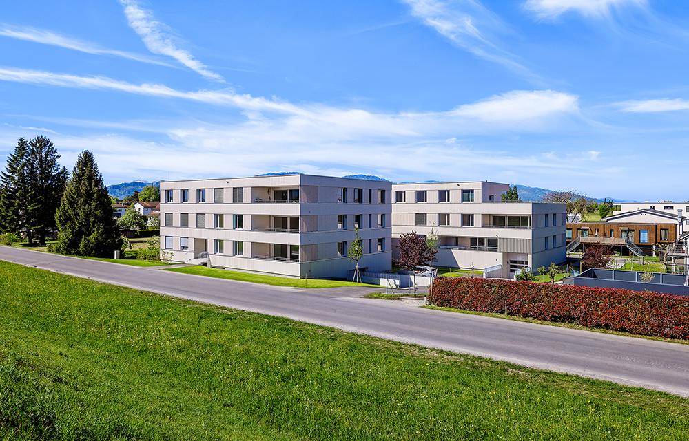 Zwei moderne Wohngebäude in ländlicher Umgebung mit viel Grün und Bergblick.
