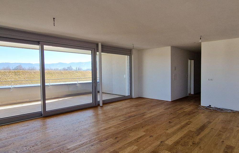 Geräumiges, unmöbliertes Wohnzimmer mit Holzboden und Zugang zu einem großen Balkon.